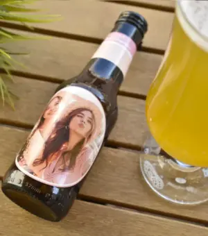 Botellín de cerveza personalizado junto a un vaso de cerveza lleno, resaltando la personalización del diseño.