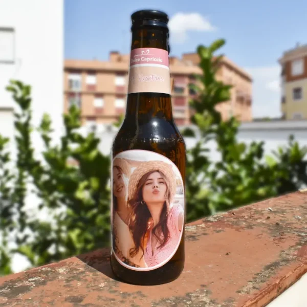 Botellín de cerveza con foto de amigas. apoyada en un poyete.