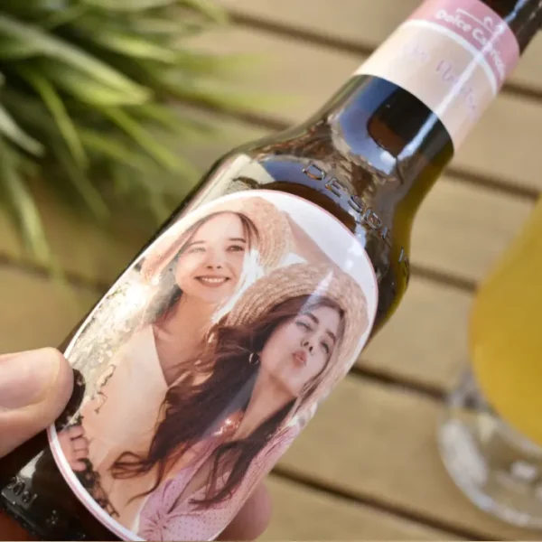 Una mano sostiene el Mano sosteniendo un botellín de cerveza personalizado con foto, enfocada en la etiqueta única y el detalle del producto.