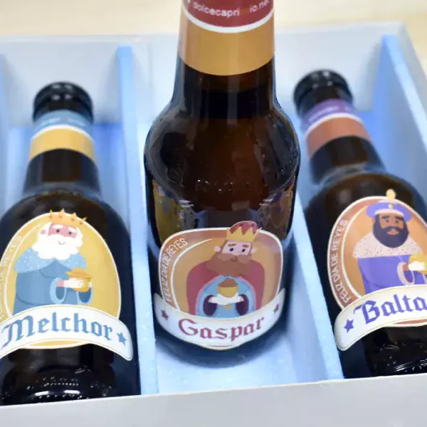 Estuche abierto y una cerveza de pie. Las cervezas caracterizadas con los Reyes Magos. El estuche viene diseñado con los tres Reyes Magos y con la frase, Oro incienso y birra.