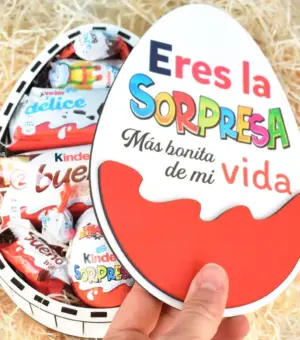 Mano abriendo una caja de madera en forma de huevo sorpresa. Se ve el interior de la caja llena de chocolates kinder.
