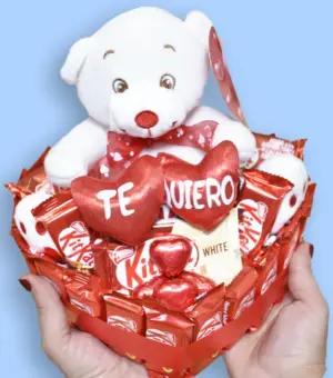 Manos sujetando una tarta de KitKat en forma de corazón con un peluche de oso con la palabra te quiero.