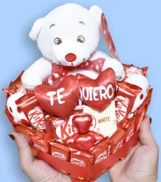 Manos sujetando una tarta de KitKat en forma de corazón con un peluche de oso con la palabra te quiero.