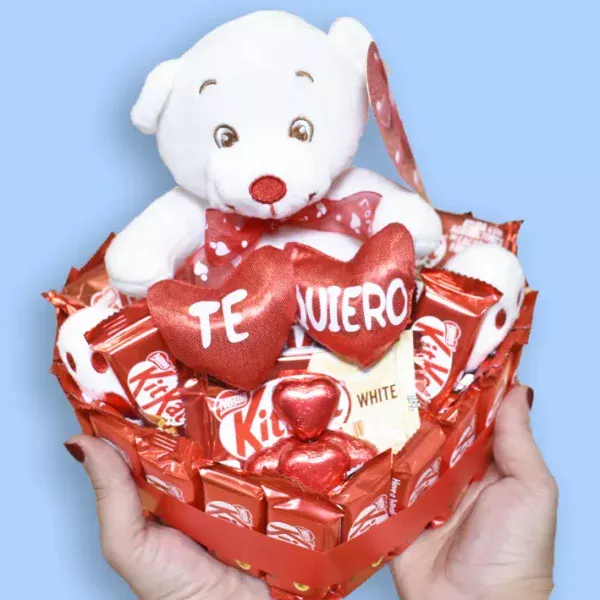 Manos sujetando una tarta de KitKat en forma de corazón con un peluche de oso con la palabra te quiero.