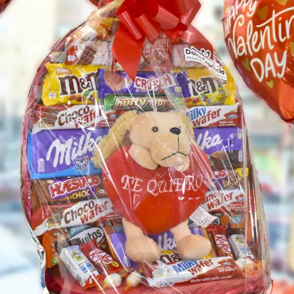 Cesta de chocolate para XL con un peluche con la palabra Te Quiero.El peluche tiene forma de perro. La cesta está envuelta con un papel celofán y lazo rojo.