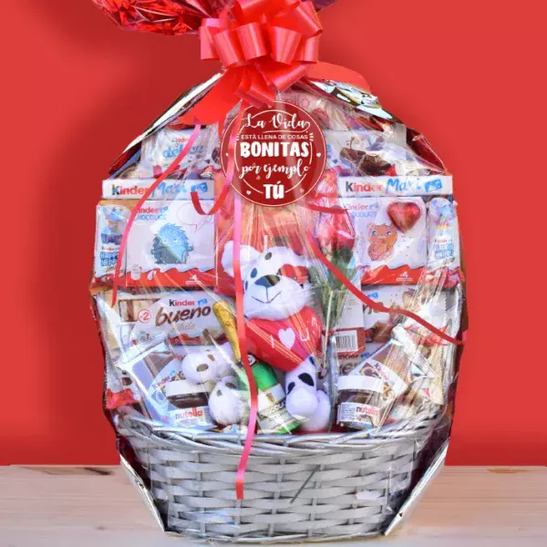 Cesta con chocolates surtidos y un peluche, ideal para regalar en San Valentín. Cerrada y envasada con un lazo rojo.